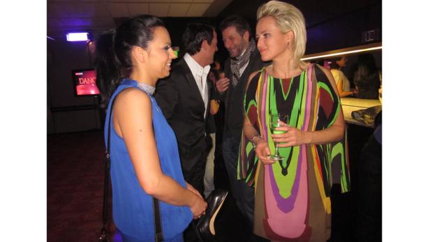 Gäste unterhalten sich auf einer Veranstaltung, eine Frau hält einen Schuh in der Hand.