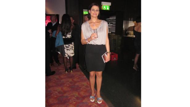 Eine Frau in einem grauen Kleid hält ein Glas in der Hand.