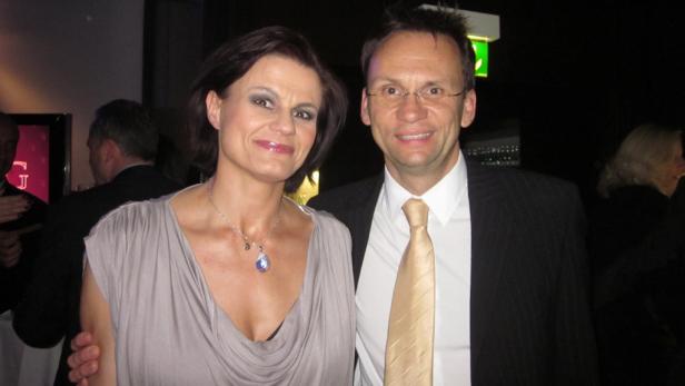 Ein Mann mit Brille und eine Frau mit Halskette posieren für ein Foto.