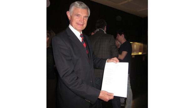 Ein Mann im Anzug hält ein Blatt Papier in der Hand.