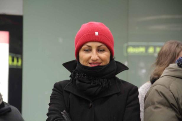 Eine Frau mit roter Mütze und schwarzem Mantel lächelt.