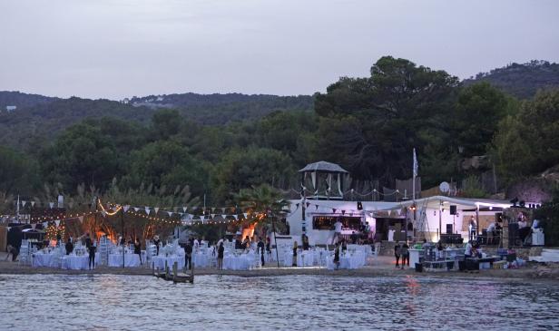 Eine abendliche Strandparty mit gedeckten Tischen und einer Bar im Hintergrund.