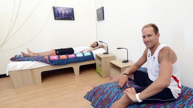 Zwei Männer in Sportkleidung ruhen sich in einem einfachen Schlafzimmer aus.