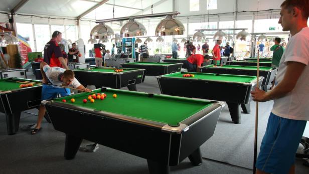 In einem Raum mit mehreren Billardtischen spielt ein Mann Billard.