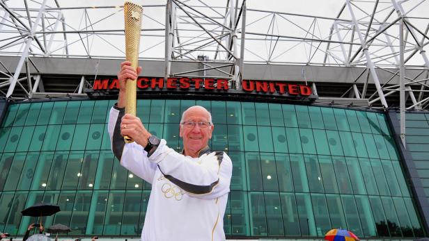 Ein Mann hält die olympische Fackel vor dem Stadion von Manchester United hoch.
