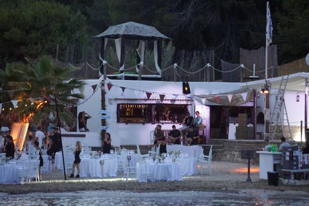 Eine Strandbar mit festlich gedeckten Tischen und Gästen im Abendlicht.