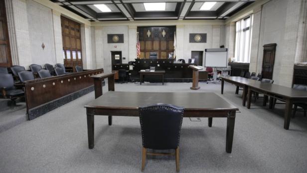 Ein leerer Gerichtssaal mit Tischen, Stühlen und der Richterbank im Hintergrund.