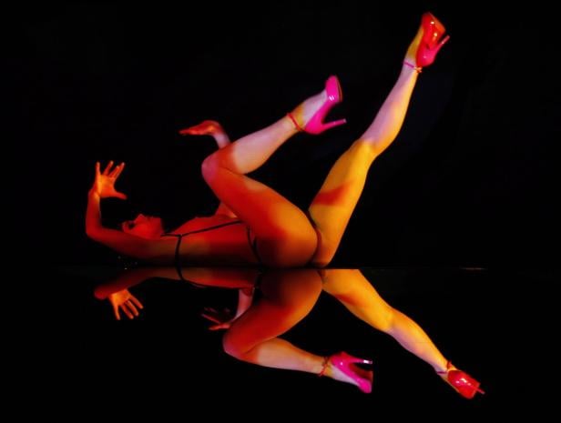 Eine Frau in Unterwäsche und pinkfarbenen High Heels posiert vor einem Spiegel.