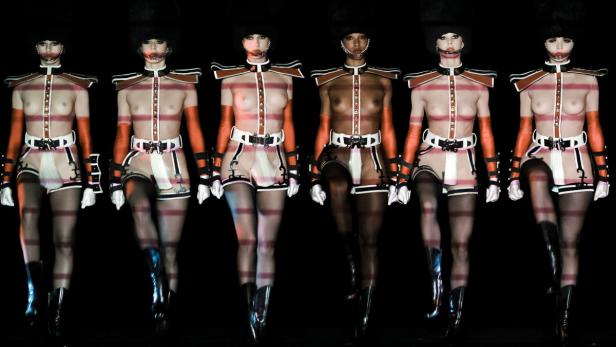 Mehrere Models in fantasievollen, freizügigen Gardeuniformen auf einem Laufsteg.