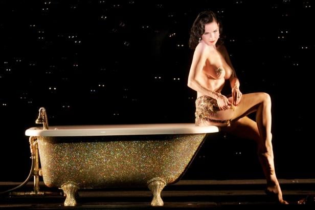 Dita Von Teese sitzt auf dem Rand einer mit Glitzer bedeckten Badewanne.