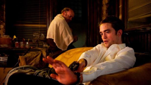 Robert Pattinson sitzt mit einer Pistole in der Hand auf einem Sofa.