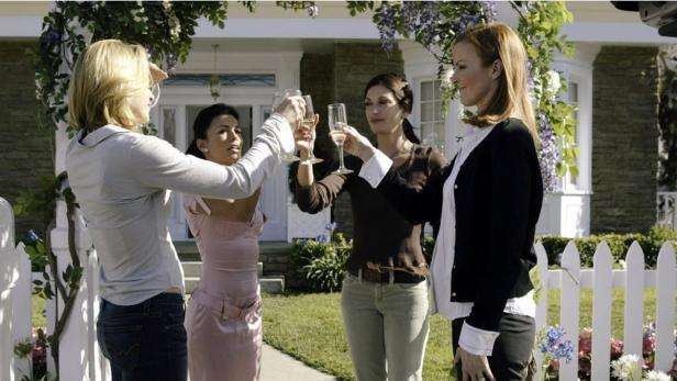 Vier Frauen stossen vor einem Haus mit Sektgläsern an.