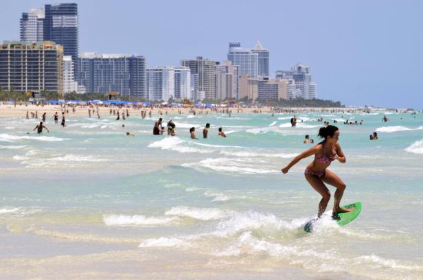 Eine Frau fährt auf einem Skimboard im flachen Wasser an einem belebten Strand.