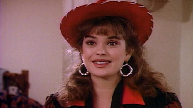 Eine Frau mit roten Cowboyhut und großen Ohrringen lächelt.