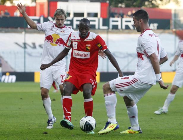 Drei Fußballspieler kämpfen um den Ball auf einem grünen Rasen.