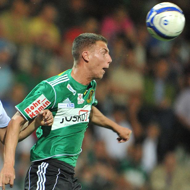 Ein Fußballspieler in einem grünen Trikot blickt auf einen Ball in der Luft.