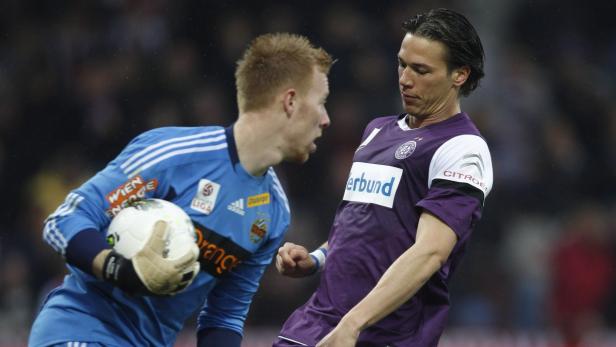 Ein Fußballspieler im lila Trikot steht einem Torwart gegenüber.