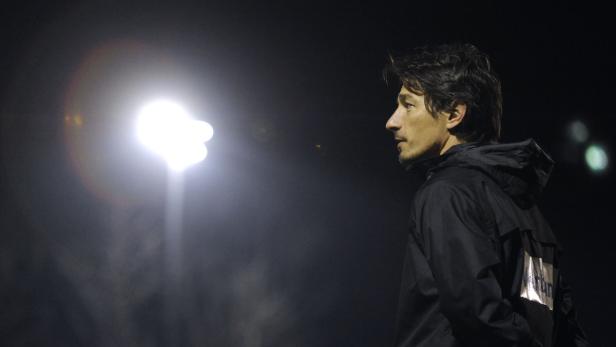 Ein Mann mit dunkler Jacke steht im Dunkeln vor einem hellen Scheinwerfer.