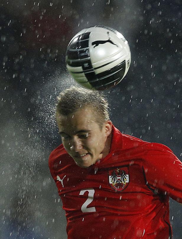 Ein österreichischer Fußballspieler köpft im Regen einen Ball.