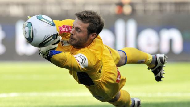 Ein Torwart in gelber Sportkleidung hechtet nach einem Fußball.