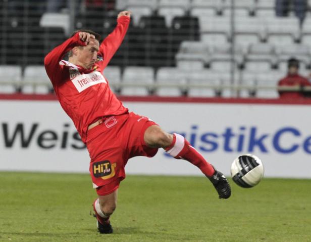 Ein Fußballspieler in roter Sportkleidung schießt einen Ball.