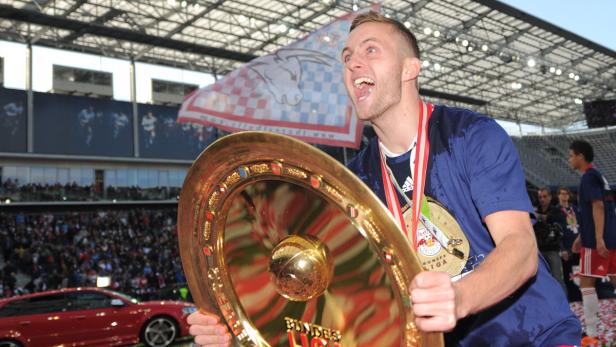 Ein jubelnder Fußballspieler hält die Meisterschale in einem Stadion.