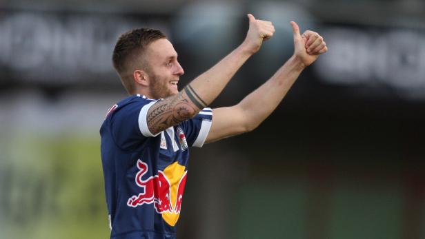 Ein lächelnder Fußballspieler mit Tattoos gibt beide Daumen nach oben.