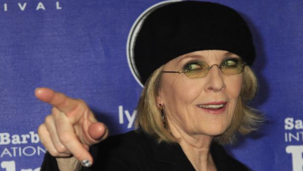 Diane Keaton mit Brille und Barett zeigt mit dem Finger auf etwas.