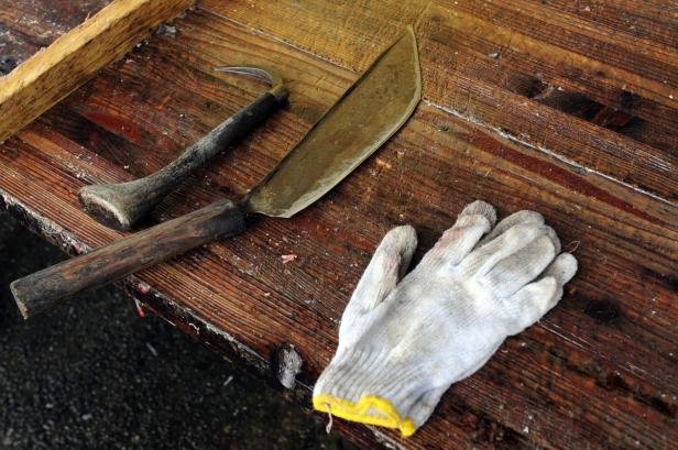 Ein Messer, ein Haken und ein Handschuh liegen auf einem Holztisch.
