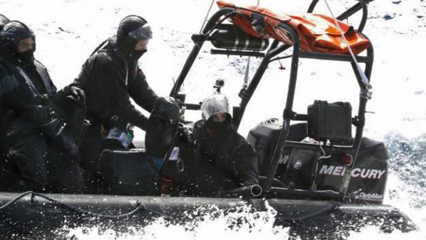 Drei Personen in dunkler Kleidung sitzen in einem kleinen Motorboot auf dem Wasser.
