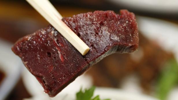 Ein Stück rohes Fleisch wird mit Essstäbchen gehalten.