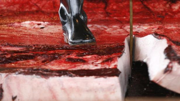 Ein Stiefel steht auf einem Stück Fleisch, das mit einem Messer geschnitten wird.