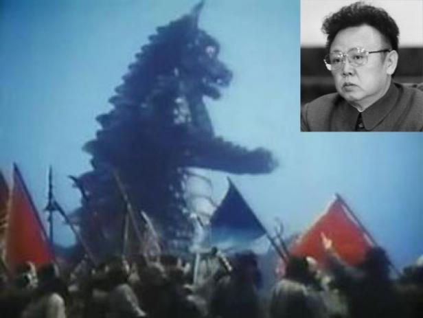 Eine Menschenmenge mit Fahnen steht vor einem riesigen Monster, im Hintergrund ein Porträt von Kim Jong-il.