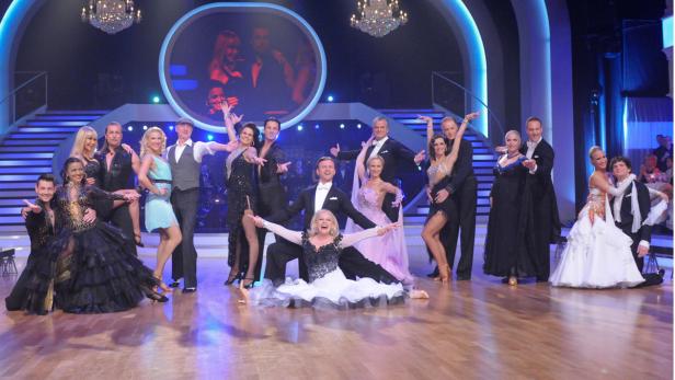 Eine Gruppe von Paaren posiert in Tanzkleidung auf einer Bühne.