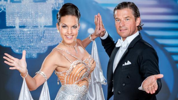 Ein Tanzpaar posiert vor einem blauen Hintergrund mit einem Kronleuchter.