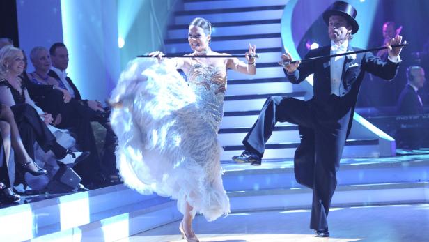 Ein Mann im Frack und eine Frau im Ballkleid tanzen auf einer Bühne.