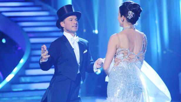 Ein Mann im Frack und eine Frau im glitzernden Kleid tanzen auf einer Bühne.
