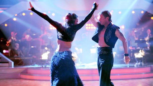 Ein Mann und eine Frau tanzen auf einer Bühne mit einer Band im Hintergrund.