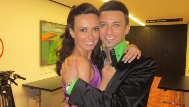 Ein Mann im Anzug und eine Frau im Kleid umarmen sich und lächeln.