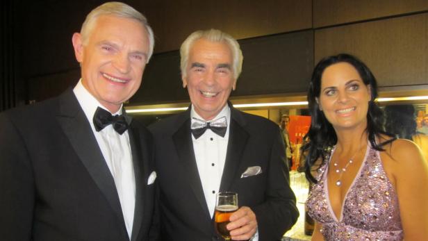 Drei Personen, gekleidet in formeller Abendgarderobe, lächeln in die Kamera.