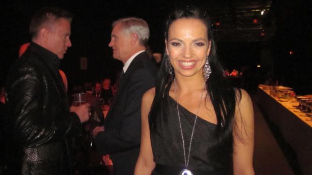 Eine lächelnde Frau in einem schwarzen Kleid auf einer Veranstaltung.