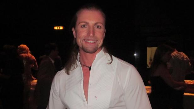 Ein Mann mit langen Haaren lächelt in einem weißen Hemd.