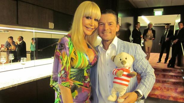 Eine Frau in einem bunten Kleid und ein Mann mit einem Teddybär posieren für ein Foto.