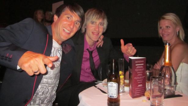 Drei Personen sitzen an einem Tisch mit Getränken und posieren für ein Foto.