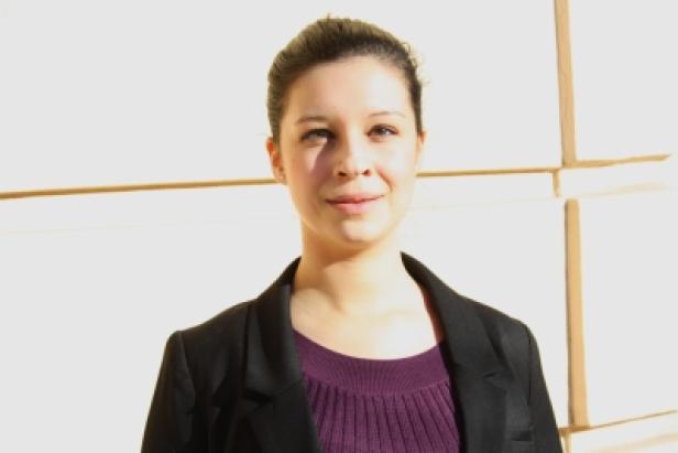 Eine junge Frau mit dunklen Haaren und einem schwarzen Blazer lächelt in die Kamera.