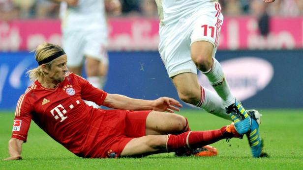 Ein Fußballspieler in roter Spielkleidung liegt auf dem Rasen, während ein anderer Spieler ihn passiert.