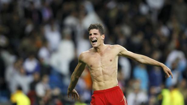 Ein jubelnder, barfüßiger Fußballspieler in roter Hose vor einer Zuschauermenge.