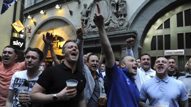 Eine Gruppe Fußballfans jubelt mit Bierkrügen vor einem Pub.