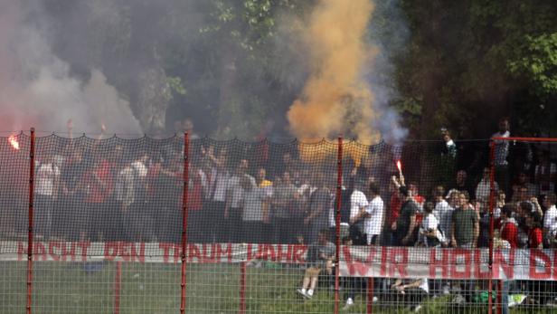 Eine Menschenmenge zündet Rauchbomben und Bengalos hinter einem Zaun.