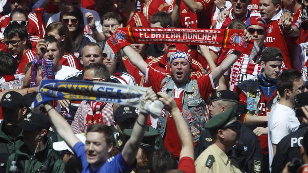 Fußballfans jubeln mit Schals von Bayern München und Chelsea im Publikum.